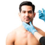 Closeup of doctor's hands injecting botox into the skin of male model on white background