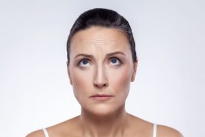Close-up of a middle-aged woman examining her forehead wrinkles, considering a brow lift for anti-aging rejuvenation and a more youthful appearance.